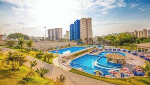 Un hotel con una grande piscina all'aperto, diverse zone relax con ombrelloni e vista sugli edifici circostanti.