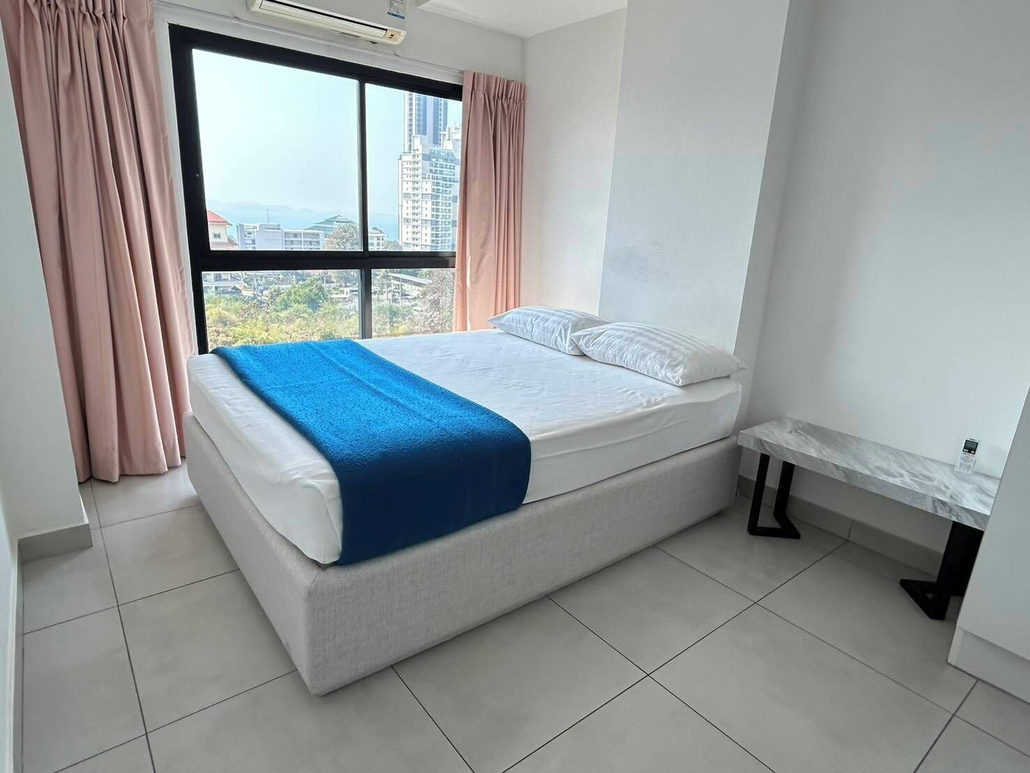 A modern bedroom with a large window, a bed with white linens and a blue blanket, and a marble bedside table.
