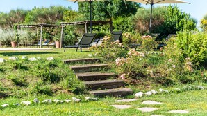 Ein Garten mit Außenbestuhlung, Steintreppe und viel Grün.