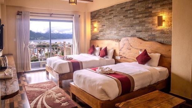 A hotel room with two beds, a wooden headboard, a large window with a view, and a stone wall. - Pinnacle Residences Pokhara (Pokhara)