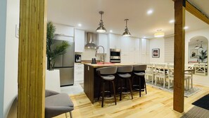Une cuisine moderne dotée d’un îlot central, de tabourets de bar et d’un coin repas avec des chaises blanches.