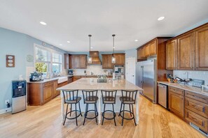 Una cocina amplia con gabinetes de madera, una isla grande con taburetes de bar y electrodomésticos de acero inoxidable.