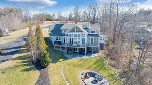 A large, two-story house with a wrap-around porch, a covered outdoor seating area, and a well-maintained lawn. - Serenity Shores - Private Lakefront Home with Dock (Moneta)