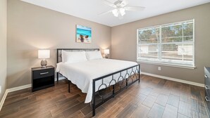 A bedroom with a bed, nightstands, a ceiling fan, a window with blinds, and a wall-mounted picture. - Downtown Gulf Shores Duplex w/ Shared Pool, Dog Friendly | BEACHBALL PROPERTIES (Gulf Shores)
