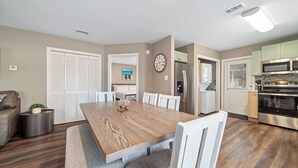A modern kitchen with a wooden dining table, white chairs, and built-in appliances. - Downtown Gulf Shores Duplex w/ Shared Pool, Dog Friendly | BEACHBALL PROPERTIES (Gulf Shores)