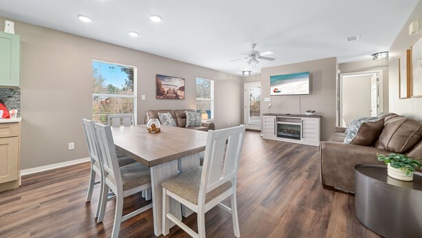 A spacious living room with a dining area, a sofa, and a TV mounted on the wall. - Downtown Gulf Shores Duplex w/ Shared Pool, Dog Friendly | BEACHBALL PROPERTIES (Gulf Shores)