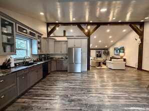 A spacious kitchen with modern appliances, a dining area with a sofa, and a view of the outdoors. - New! Spacious Lodge | 3 Kings | Hot Tub & Fire Pit (Whitefish)