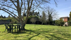 A grassy outdoor area with a tree, a table with chairs, and a building in the background. - Cozy house near the beach of Meirás. (Montefaro (Meiras))