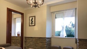 A cozy room with a stone accent wall, a large window with a view, a chandelier, and a framed artwork. - Cozy house near the beach of Meirás. (Montefaro (Meiras))