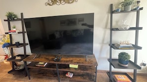 Ett vardagsrum med en stor TV med platt skärm, ett träbord och svarta hyllsystem med dekorativa föremål.
