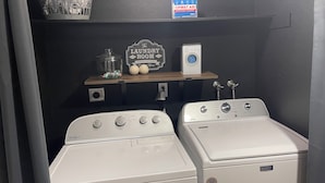 Ett tvättrum med två tvättmaskiner som man fyller på framifrån, en hylla med ett första hjälpen-kit, en korg och en skylt som visar att det är ett tvättrum.