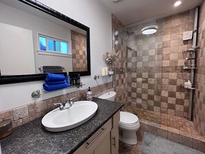 Et badeværelse med vask med granitbordplade, et hvidt toilet og en brusekabine med glasvægge.