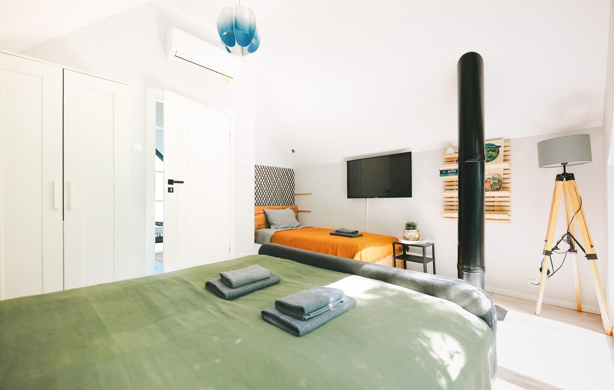 A modern bedroom with a bed, a TV, a tripod lamp, and a wardrobe.