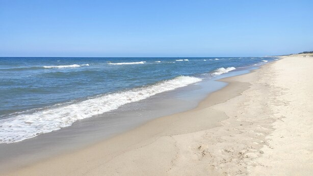 Ein Strand mit weitem Sandstrand und sanften Wellen.