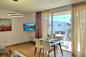 Un saló modern amb zona de menjador, televisió de pantalla plana i una finestra gran amb cortines.