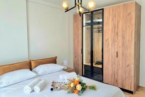 A neatly made bed with white linens, a wooden wardrobe, and a bedside table with a lamp. - SanPietro Holiday Homes 293, Lalzit Bay, Albania (Lalzit Bay)
