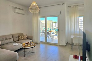 Ein Wohnzimmer mit einer Couch, einem Couchtisch mit Frühstücksgebäck, einem Fernseher und einer Glastür zu einem Außenbereich.