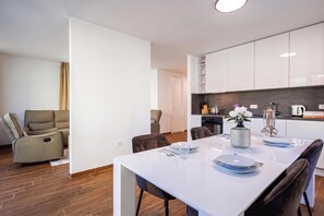 A modern kitchen with white cabinets, a dining table set for two, and a sofa in the adjacent living area. - Luxury City Penthouse Adialuxe S7, Rijeka, Croatia (Rijeka)