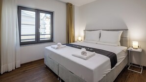 A neatly made bed with a black towel and a towel with a logo, a bedside table with a lamp, and a window with curtains. - Luxury City Penthouse Adialuxe S7, Rijeka, Croatia (Rijeka)