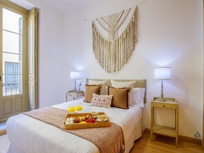 Ein Hotelzimmer mit einem Bett, Nachttischen, einem Wandbehang aus Makramee und einem Frühstücksbrett auf dem Bett.