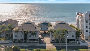 Un hotel frente a la playa con edificios de varios pisos, un estacionamiento y palmeras.