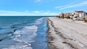 Una playa con una extensa franja de arena y una hilera de edificios con balcones y techos rojos.