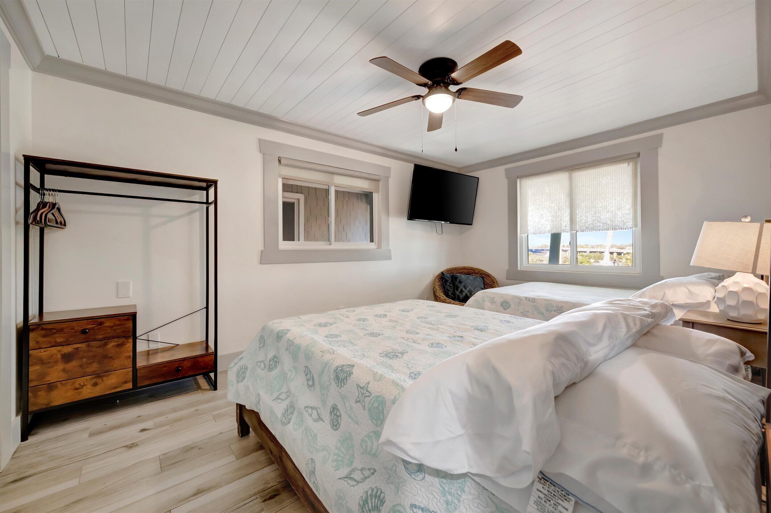 A bedroom with two beds, a ceiling fan, a TV mounted on the wall, and a wooden dresser.