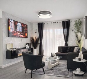 A modern living room with a flat-screen TV, black sofas, a coffee table, and a fireplace. - Modern 2-BR Apt. in Boca Chica l 5 min from the Airport 6 mins from beaches (Boca Chica)