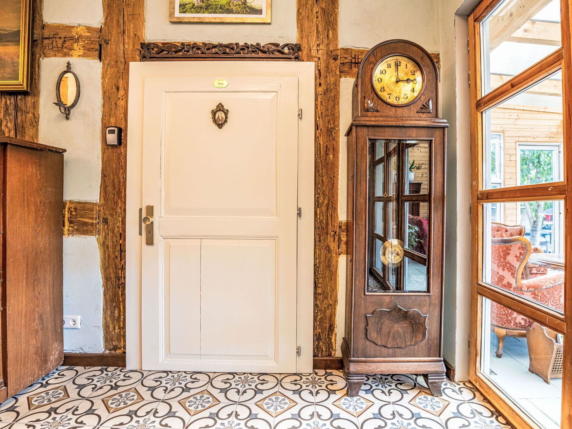 A white door with a brass handle, a wooden grandfather clock, and a patterned tile floor.