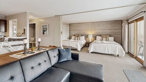 Ett hotellrum med en stor säng, en mindre säng, en soffa, en matplats och utsikt genom en skjutdörr.