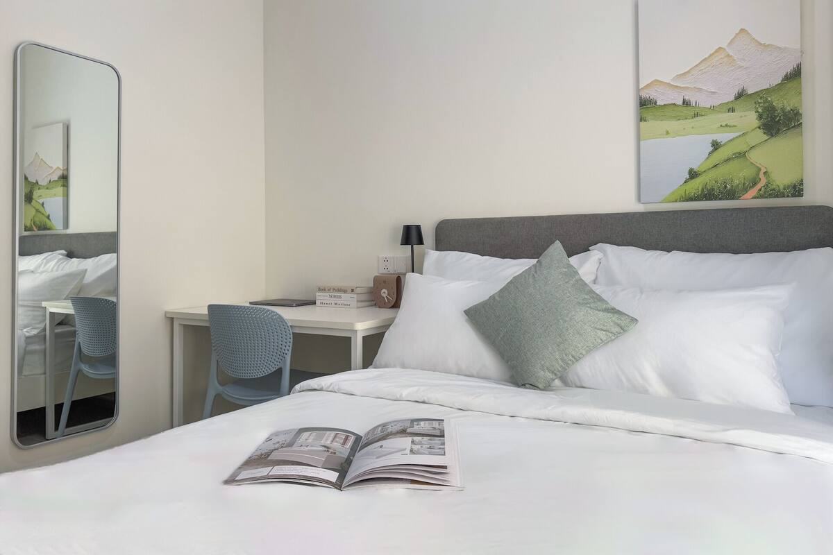 Ein Hotelzimmer mit einem Bett, einem Schreibtisch, einem Stuhl, einem Spiegel und einem Gemälde an der Wand.