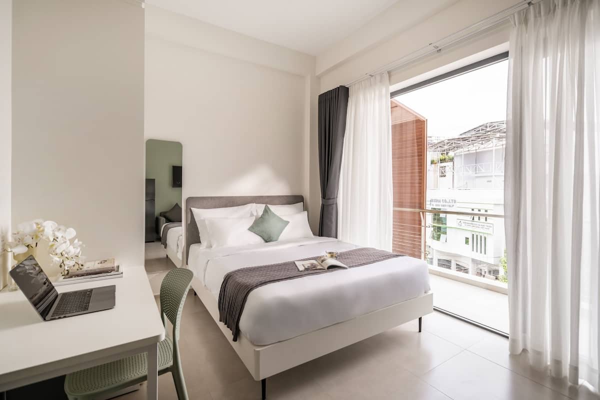 Ein modernes Hotelzimmer mit Bett, Schreibtisch, Laptop, Stuhl und Blick ins Freie.