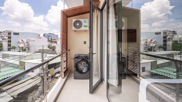 A balcony with a washing machine, a sliding glass door, and a view of the cityscape. - CityHouse NEST Bellita (Ho Chi Minh City)