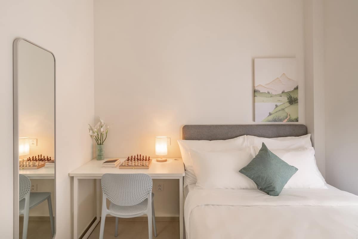 Ein Hotelzimmer mit einem Bett, einem Schreibtisch mit Schachbrett, einem Sessel und einem Bild an der Wand.