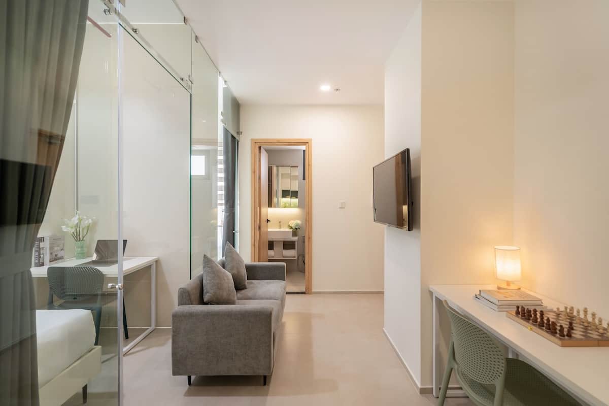 Ein modernes Hotelzimmer mit Glastrennwand, einer Couch, einem Schreibtisch mit Lampe und einem Schachbrett.