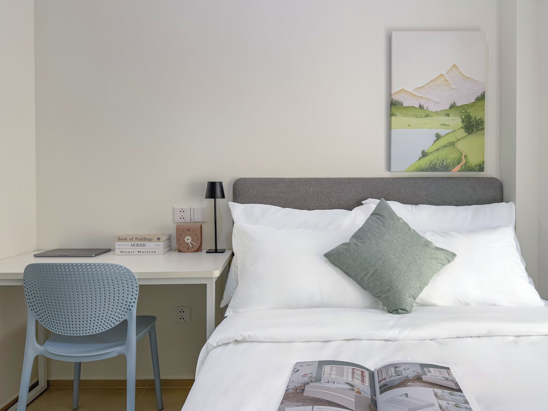 A neatly arranged hotel room with a bed, a desk, a chair, a lamp, and a painting on the wall.