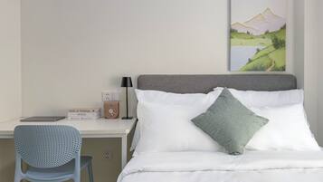 A neatly arranged hotel room with a bed, a desk, a chair, a lamp, and a painting on the wall.