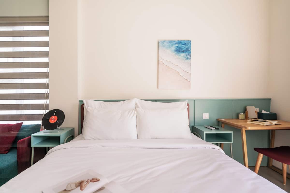 Ein Hotelzimmer mit Bett, Schreibtisch, Stuhl, einer Uhr und einem Gemälde an der Wand.