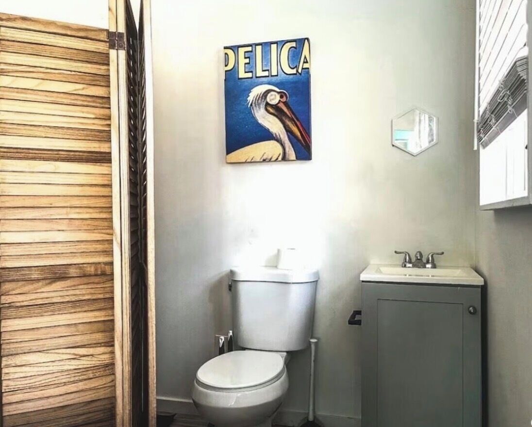 Une salle de bain comprenant des toilettes, un lavabo et une œuvre d’art fixée au mur représentant un pélican.
