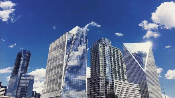 A cityscape with modern skyscrapers, clear blue sky, and scattered clouds.