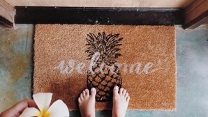 A doormat with a pineapple design and the word "Welcome" on a brown mat.