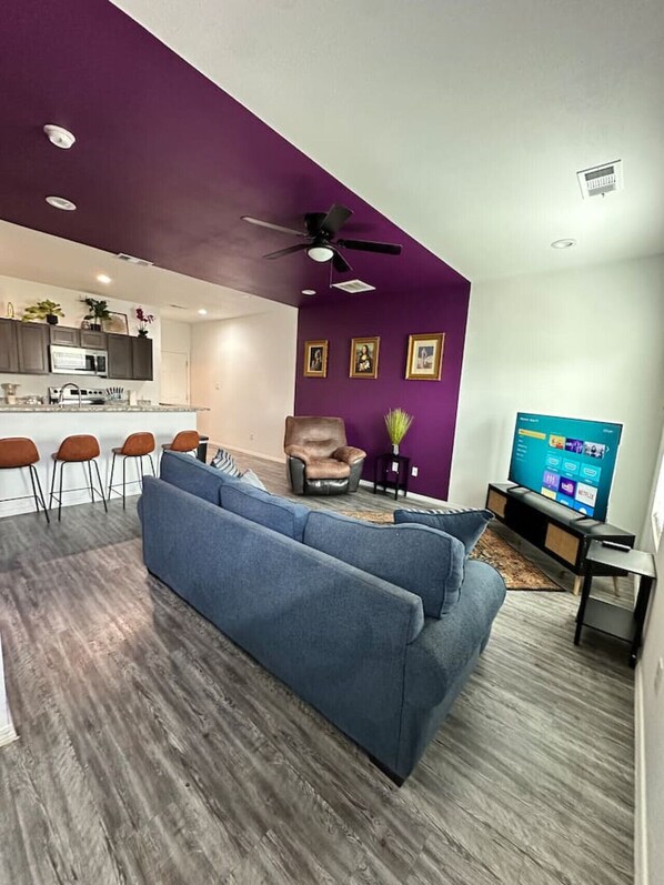 Una sala moderna con un sofá, un televisor y un comedor con taburetes de bar.
