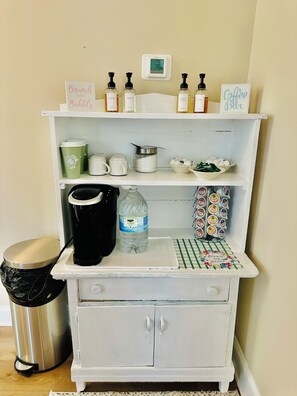 Una kitchenette equipada con cafetera, dispensador de agua y cápsulas de café en la alacena.