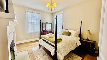 Un dormitorio con cama con dosel, mesita de noche, lámpara, cómoda, espejo y ventana con persianas.