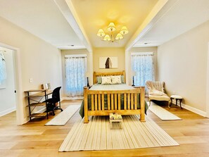Un dormitorio con una cama de madera, un escritorio, una silla, un taburete pequeño y una araña.