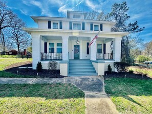 A two-story house with a front porch, a flag, and a driveway leading to the entrance.