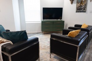 Una sala de estar moderna con televisor de pantalla plana, cómoda verde y sofás de cuero negro con cojines amarillos.
