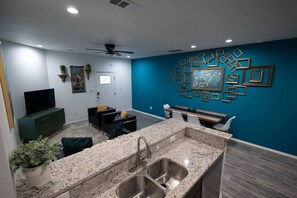 Una cocina moderna con encimeras de granito, pileta de acero inoxidable y una zona de comedor con mesa y sillas de madera.