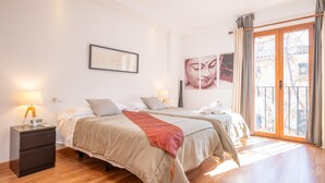 A bedroom with two beds, a nightstand, a lamp, and a large window with curtains.