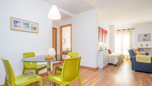 A modern living room with a glass dining table, bright green chairs, a blue sofa, and a wooden floor.